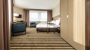 Une chambre d’hôtel avec un lit, un bureau, une chaise et une grande fenêtre avec des rideaux.