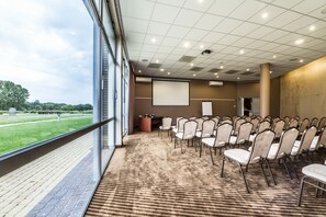 Une salle de conférence dotée d’un grand écran, de rangées de chaises et d’un sol recouvert de moquette.