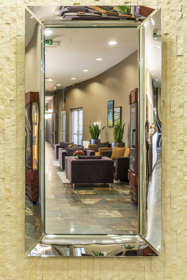 A hotel lobby with a large mirror, seating area, and potted plants. - Hotel Victor Pruszków DeSilva (Pruszkow)