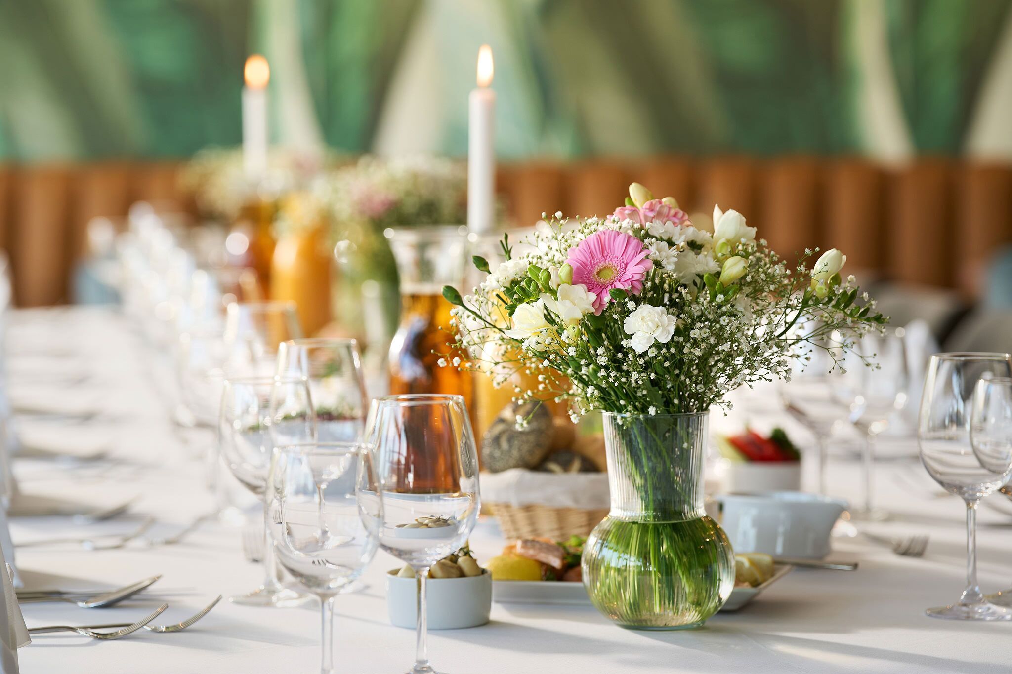 A table set with wine glasses, a centerpiece with flowers, and candles.