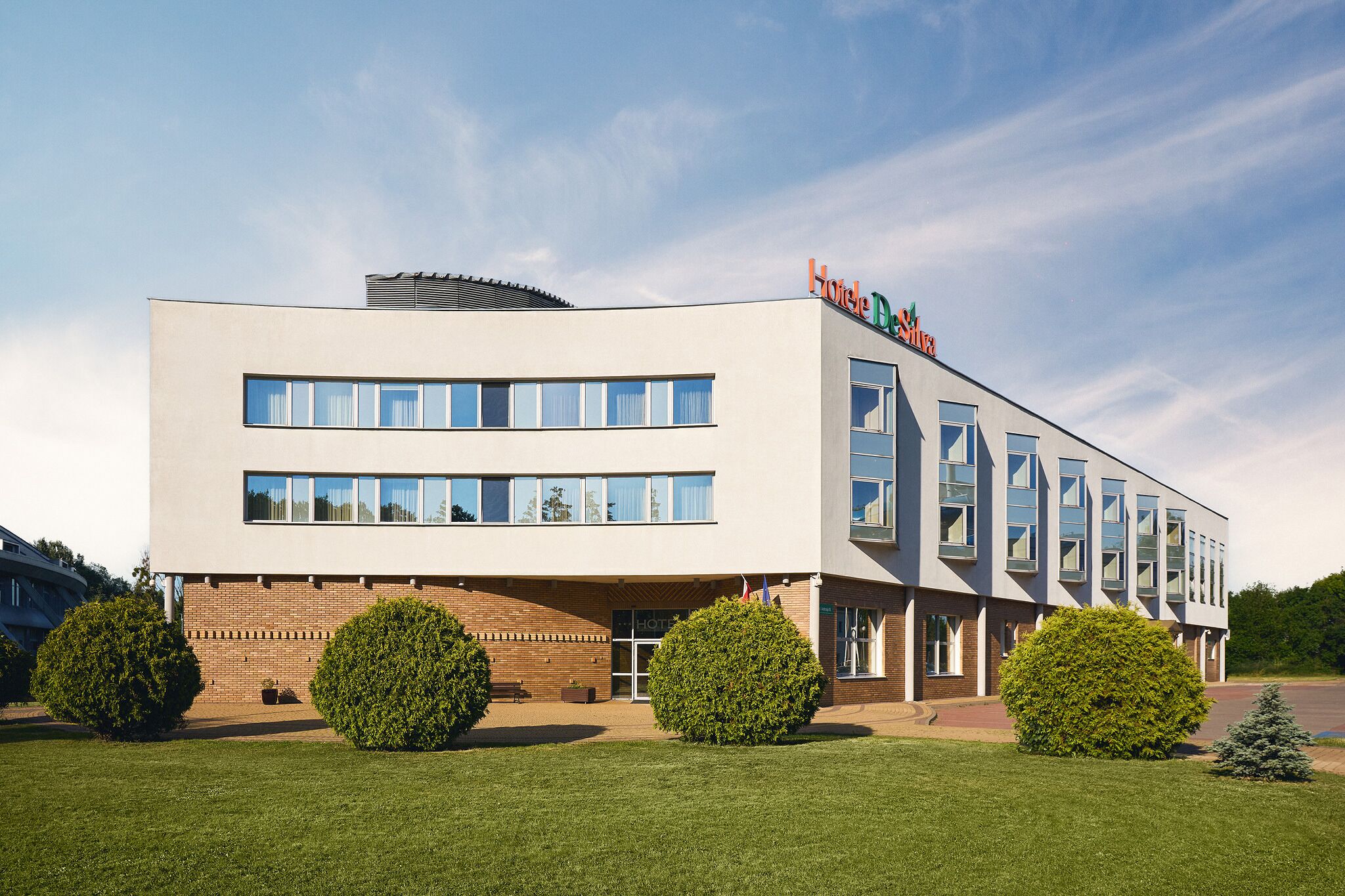 Ein modernes Hotelgebäude mit flachem Dach, zahlreichen Fenstern und einem Schild mit der Aufschrift 'Hotel Desilva'.