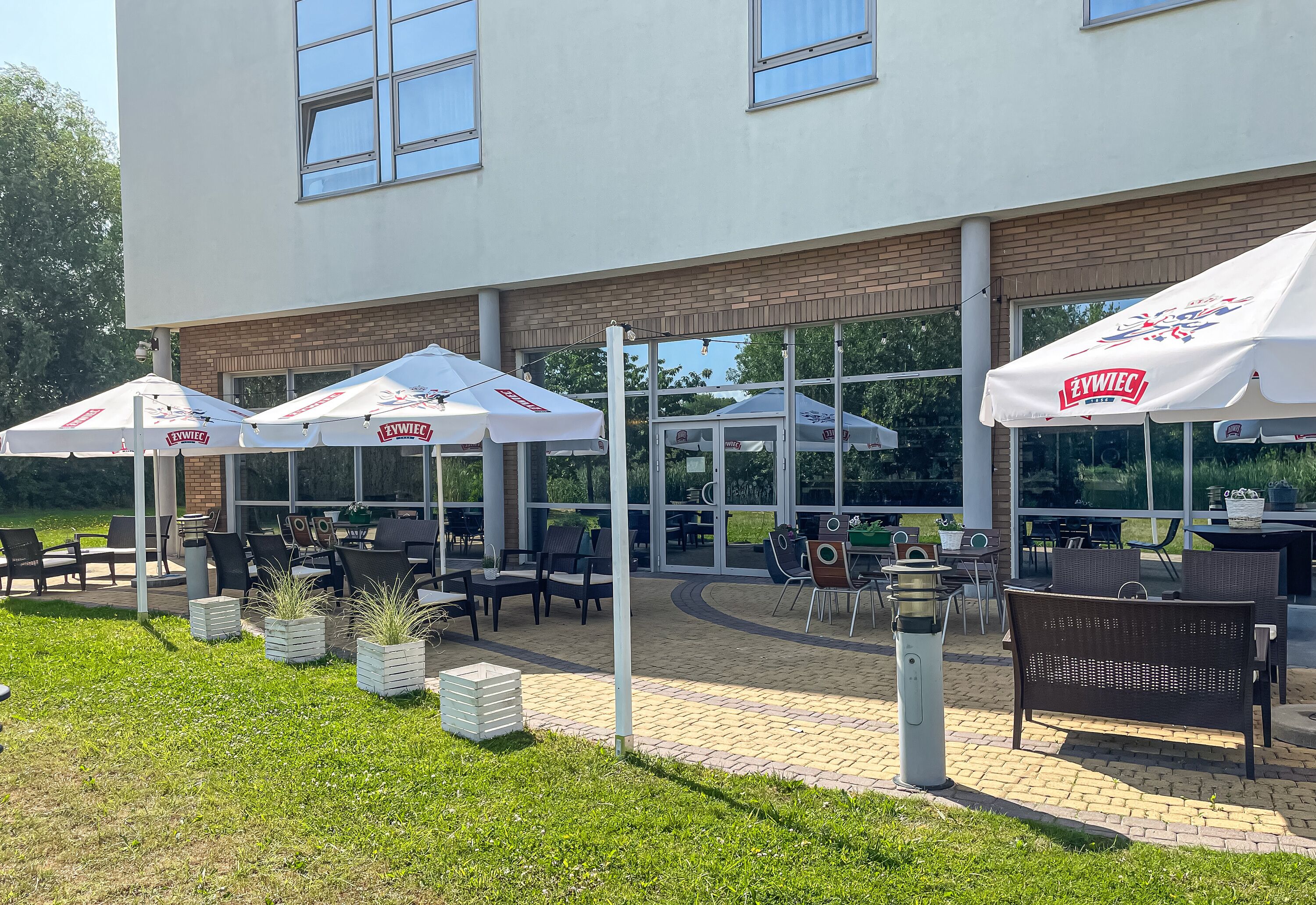 An outdoor patio area with tables and chairs under white awnings, a brick pathway, and a grassy area.