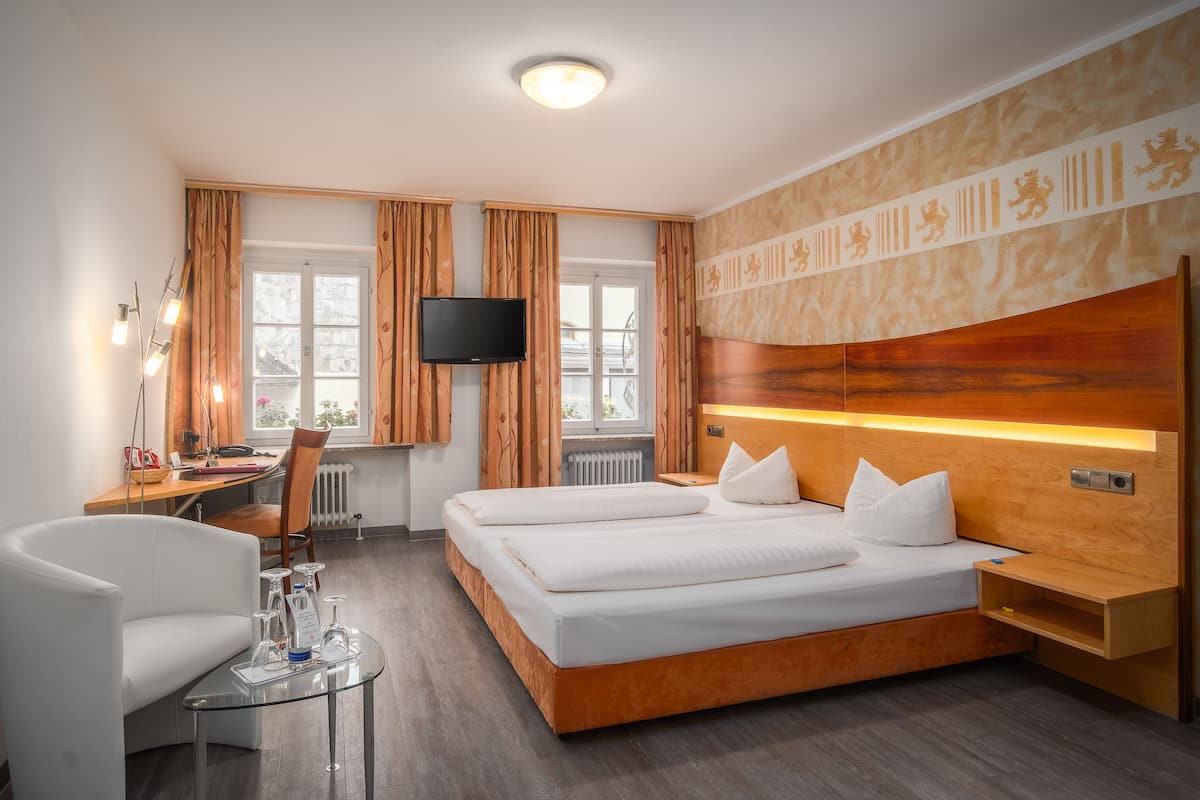 Una habitación de hotel moderna con un cabecero de madera, un televisor de pantalla plana montado en la pared, un escritorio con una silla y una mesa de centro de vidrio.