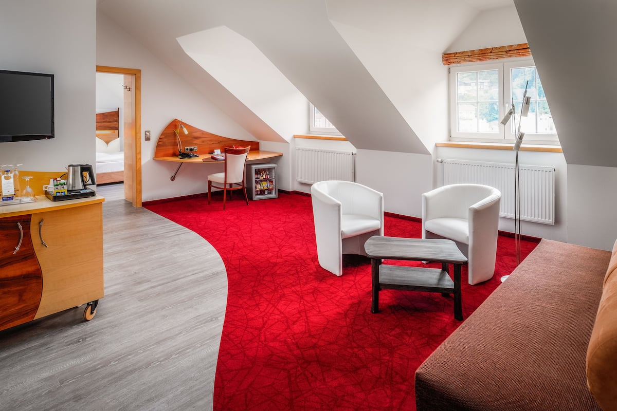 Una habitación moderna con alfombra roja, muebles blancos y un televisor fijado a la pared.