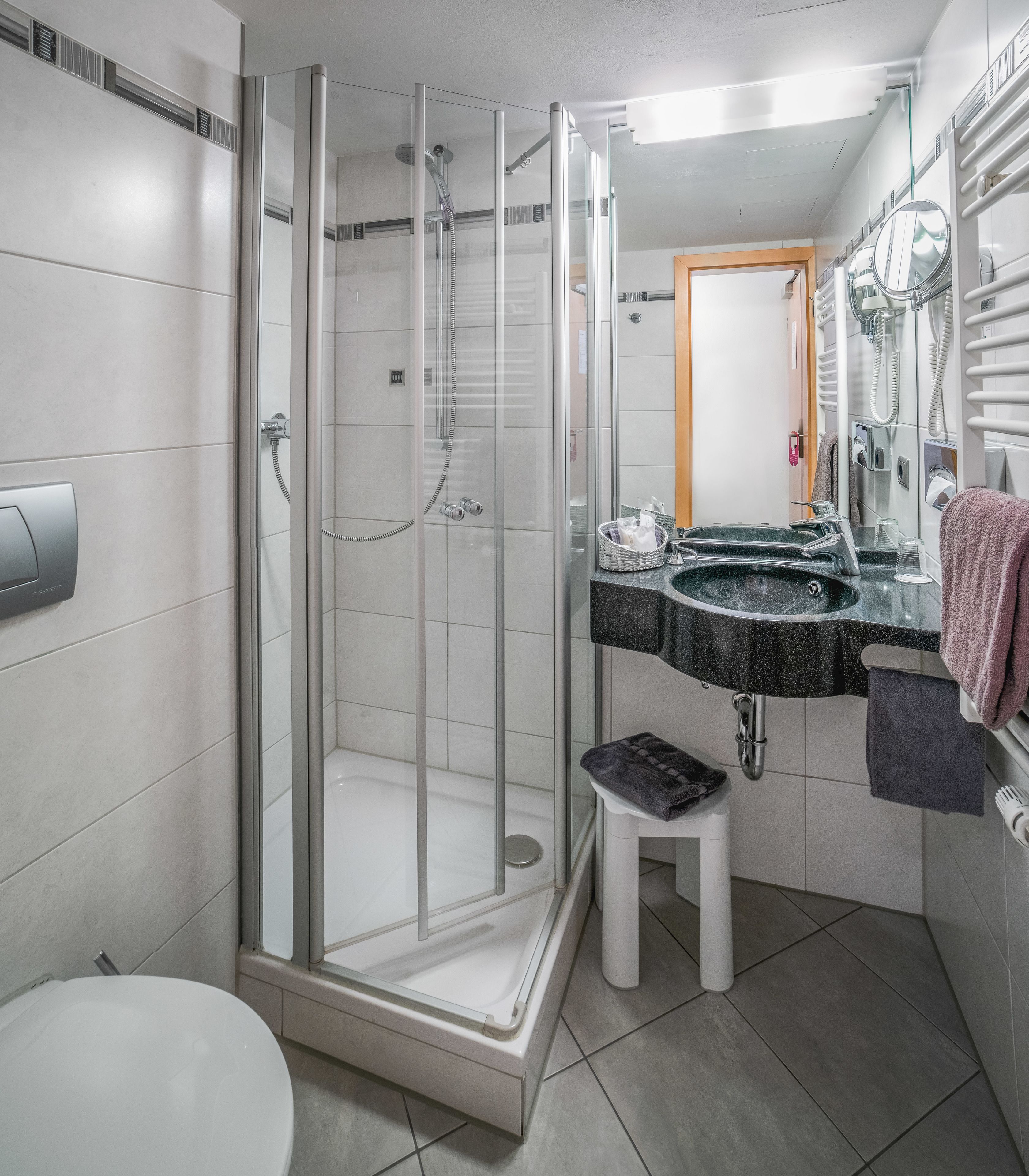 A modern bathroom with a glass-enclosed shower, a white toilet, a sink with a mirror, and a towel rack.