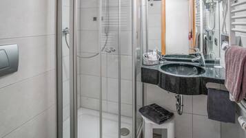 A modern bathroom with a glass-enclosed shower, a white toilet, a sink with a mirror, and a towel rack.