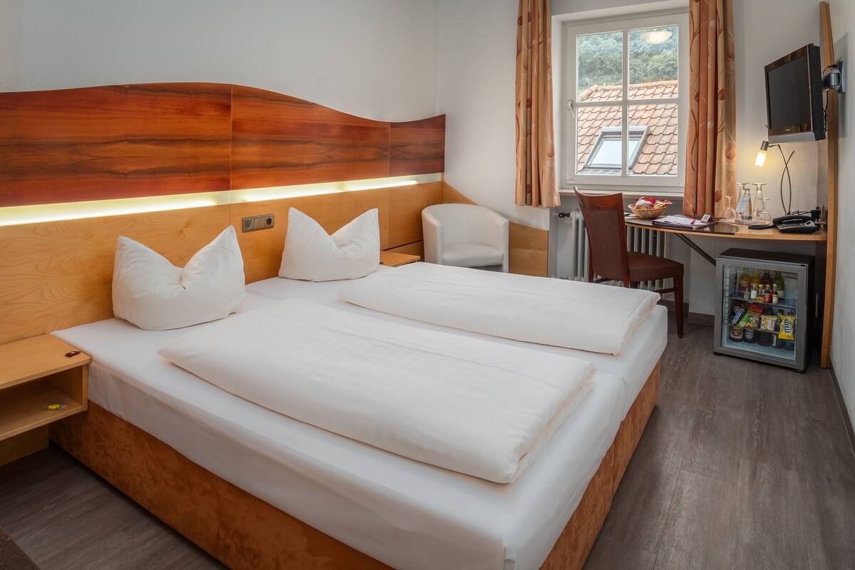 Habitación de hotel con dos camas, cabecera de madera, escritorio con silla, televisor y minibar.