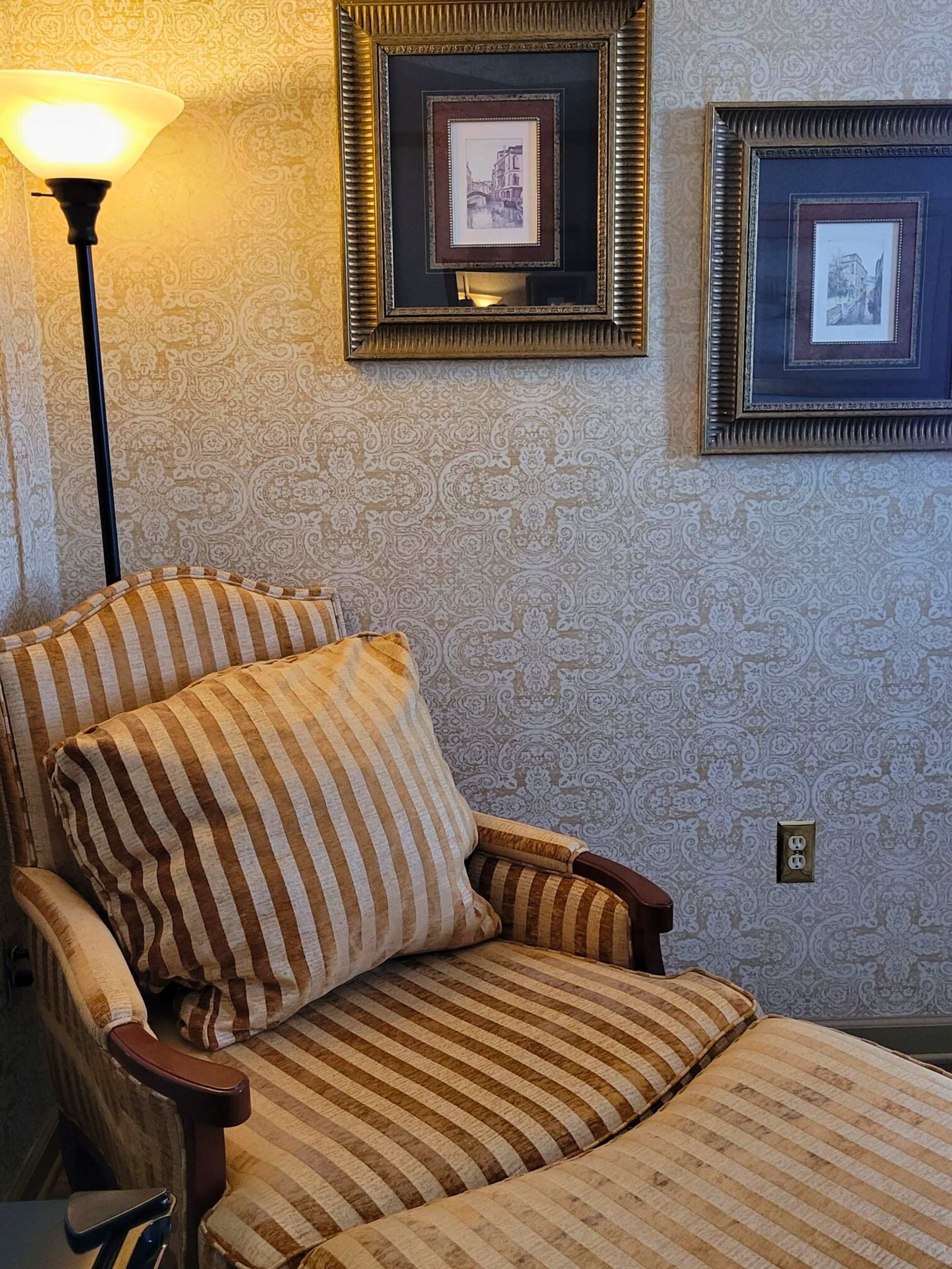 A striped armchair with a cushion, a lamp, and two framed pictures on the wall.