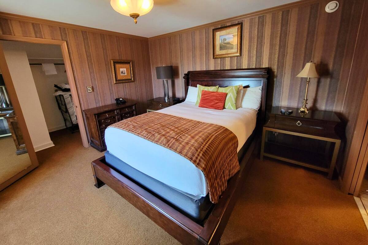 A hotel room with a large bed, wooden paneling, a desk with a lamp, and a picture on the wall.