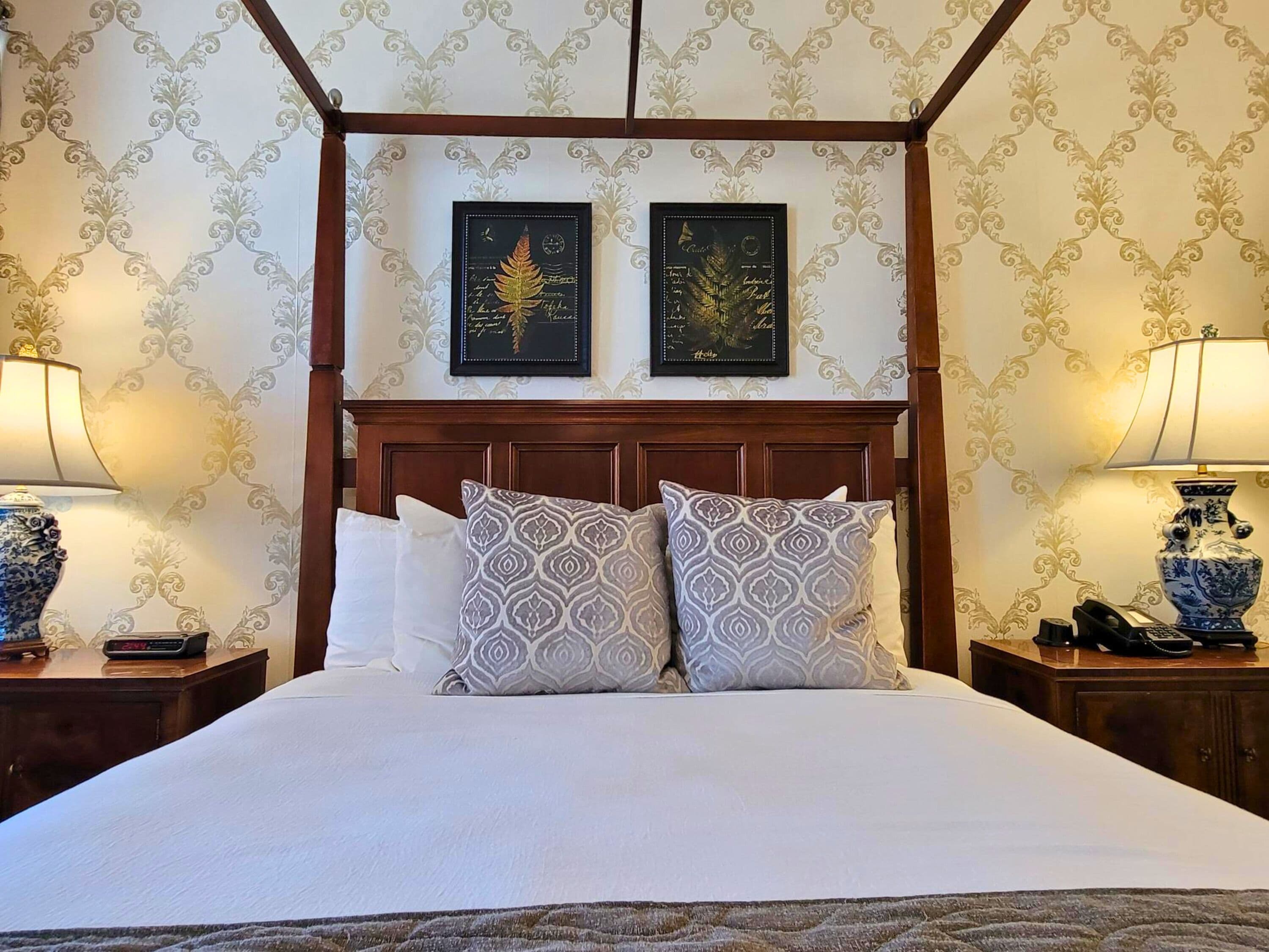A neatly made bed with patterned pillows, a wooden headboard, and two framed artworks above it.