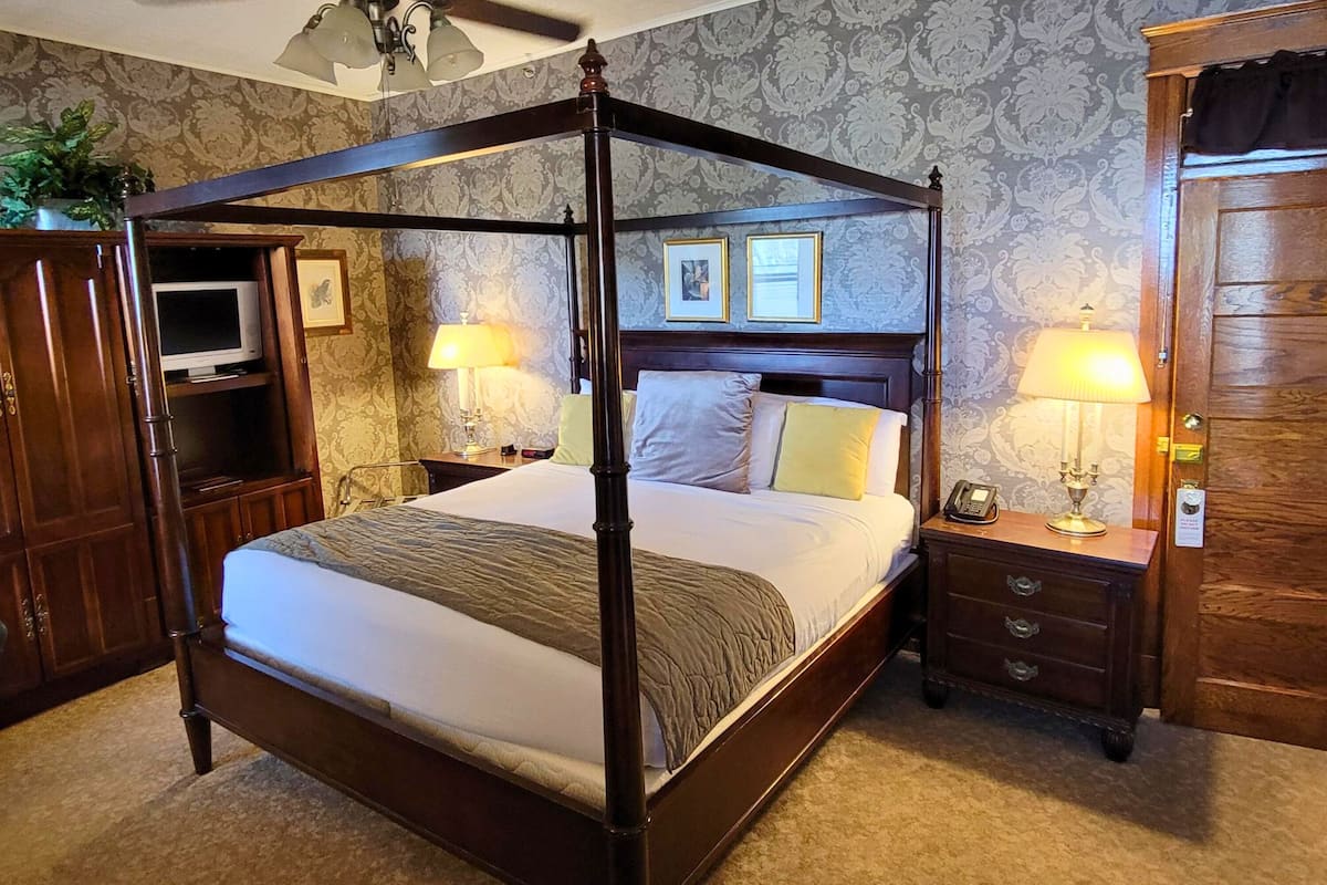 A four-poster bed with a ceiling fan, bedside lamps, and a TV on a cabinet.