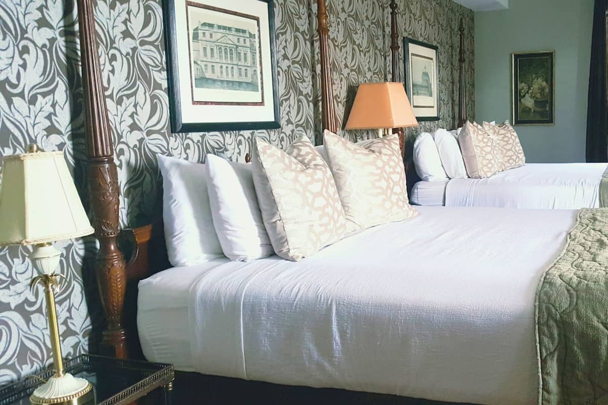 A hotel room with two beds, a nightstand with a lamp, and framed pictures on the wall.