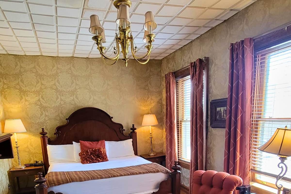 A hotel room with a large bed, a sitting area with a chair, a round table, and a chandelier.
