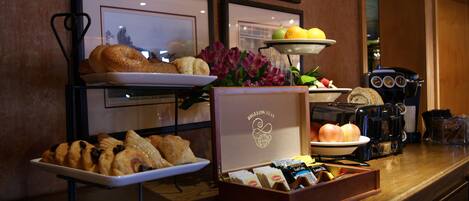 A breakfast buffet with pastries, fruits, and a coffee machine.