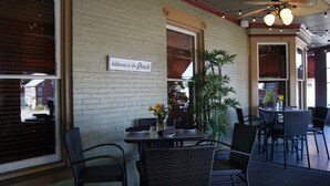Een terras met rieten stoelen en tafels, een bord met daarop 'Welcome to the Porch' en een plafondventilator.
