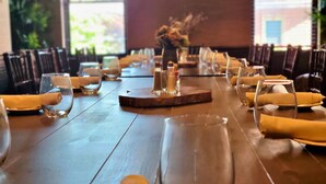 Een lange eettafel met stoelen, glazen en servetten, en een bloevas in het midden.