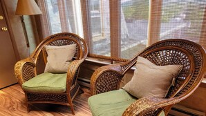 Twee rieten stoelen met kussens, geplaatst bij een raam met luiken.