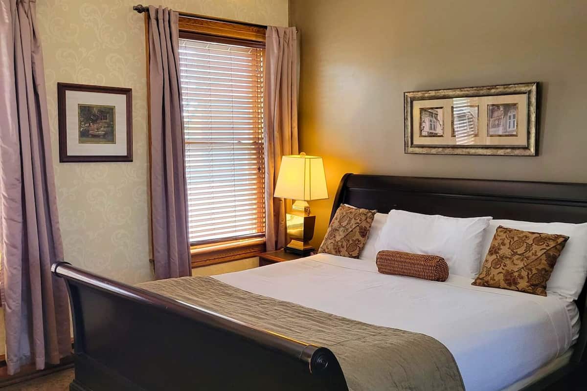 A neatly made bed with a dark headboard, a bedside lamp, and a framed picture on the wall.