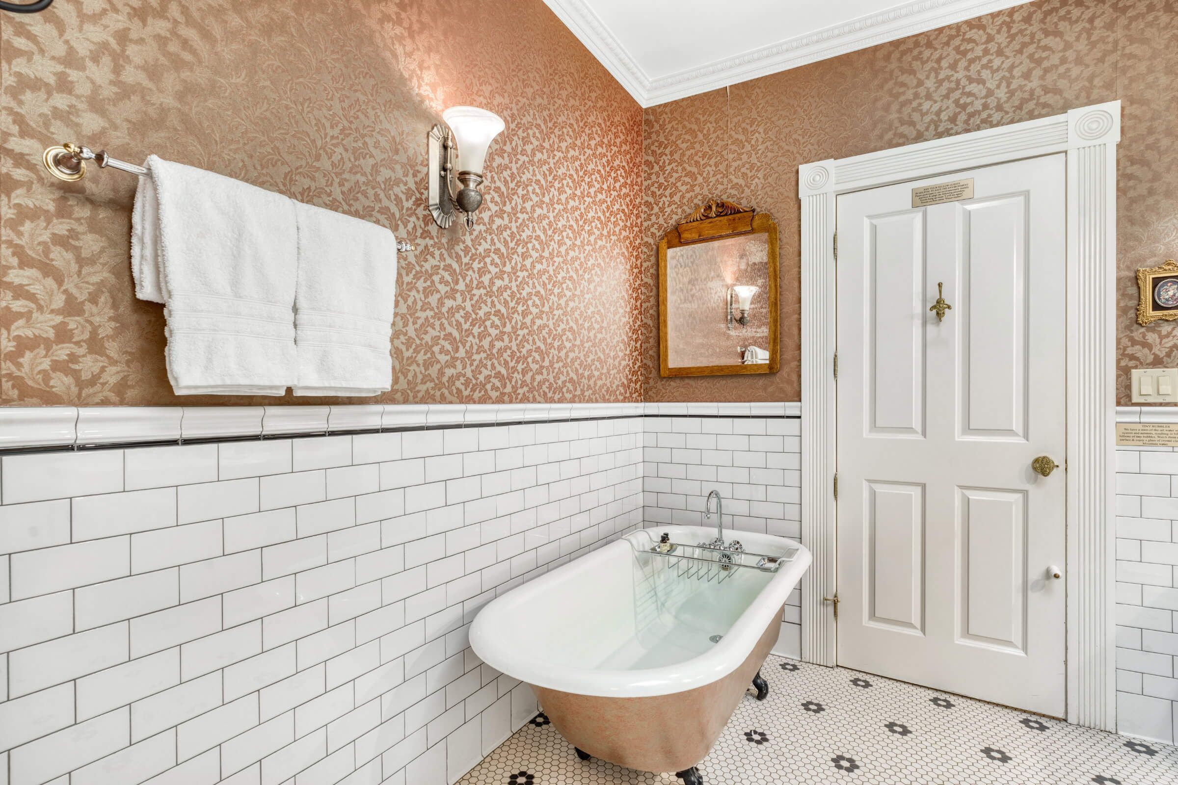 Une salle de bain avec une baignoire sur pieds, des murs recouverts de carreaux blancs et un papier peint à motifs.