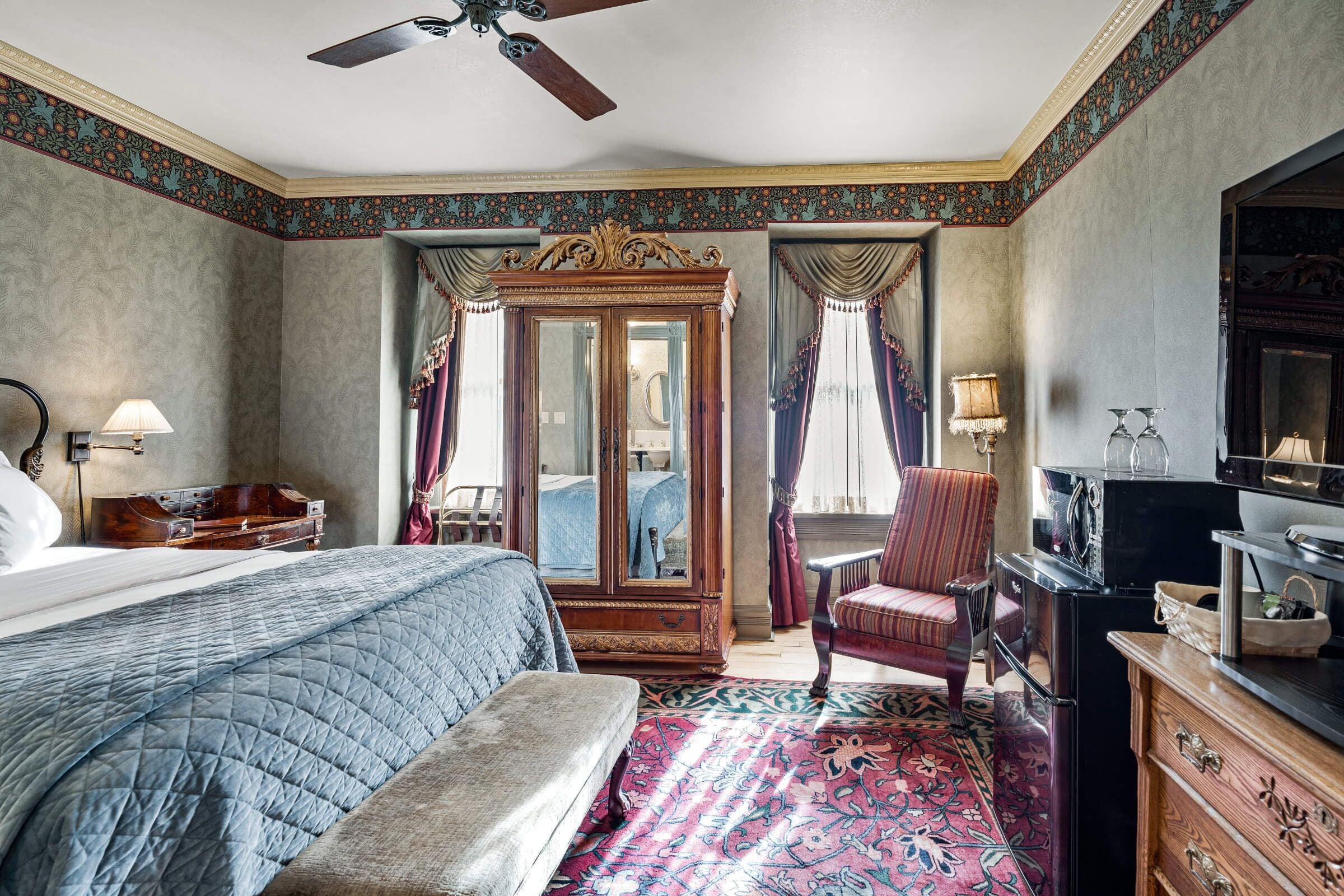 A bedroom with a large bed, a wardrobe, a chair, a desk, and a television.