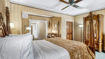 Quarto de hotel com uma cama grande, um ventilador de teto, um guarda-roupa de madeira e uma mesa com abajur.