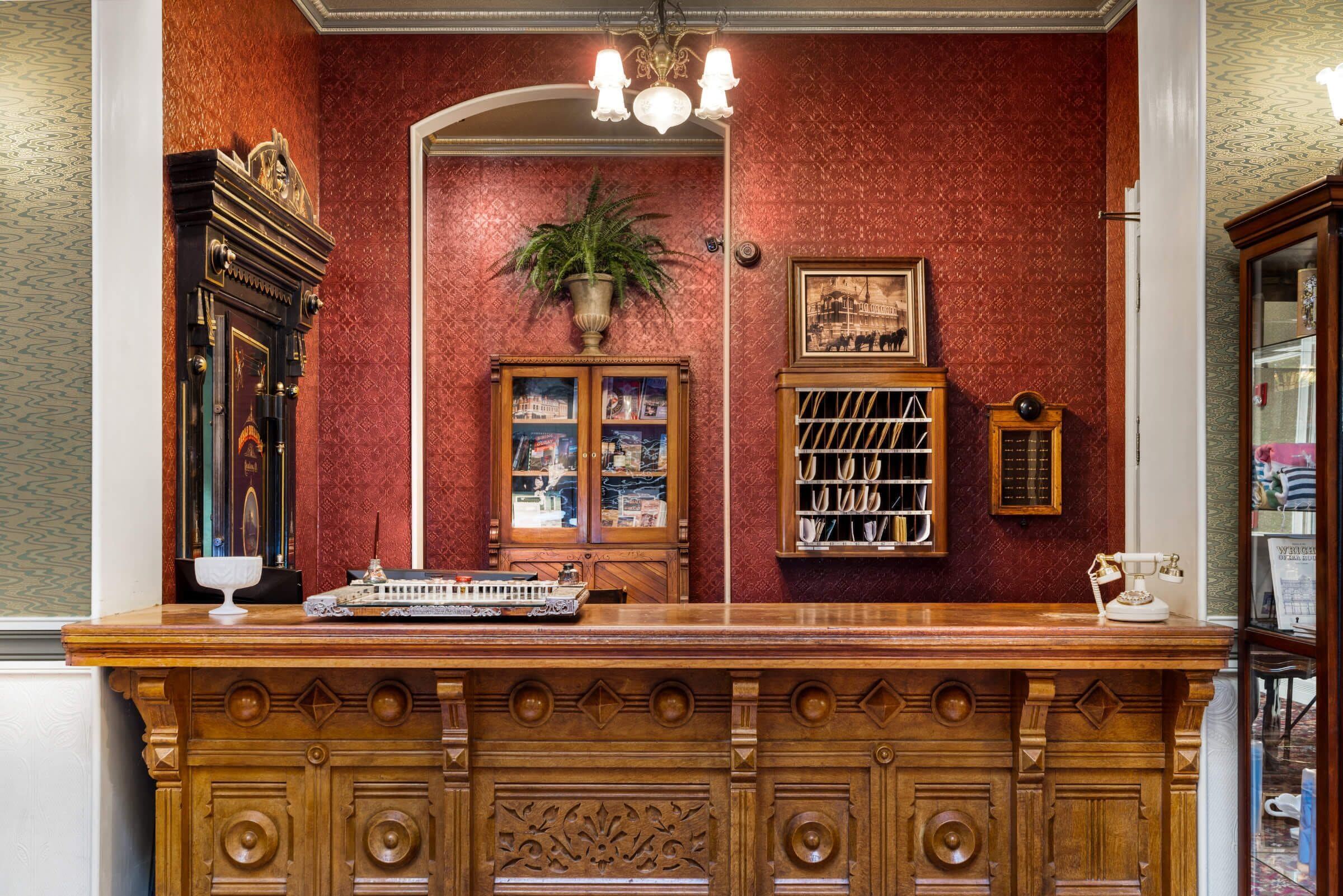 A reception area with a wooden counter, a potted plant, a framed picture, and a vintage telephone.