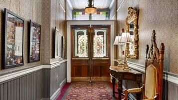 A hallway with a patterned carpet, wooden doors with stained glass, a mirror, and framed pictures on the wall.