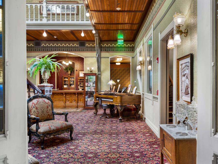 A grand lobby with a piano, a large armchair, and a bookshelf.