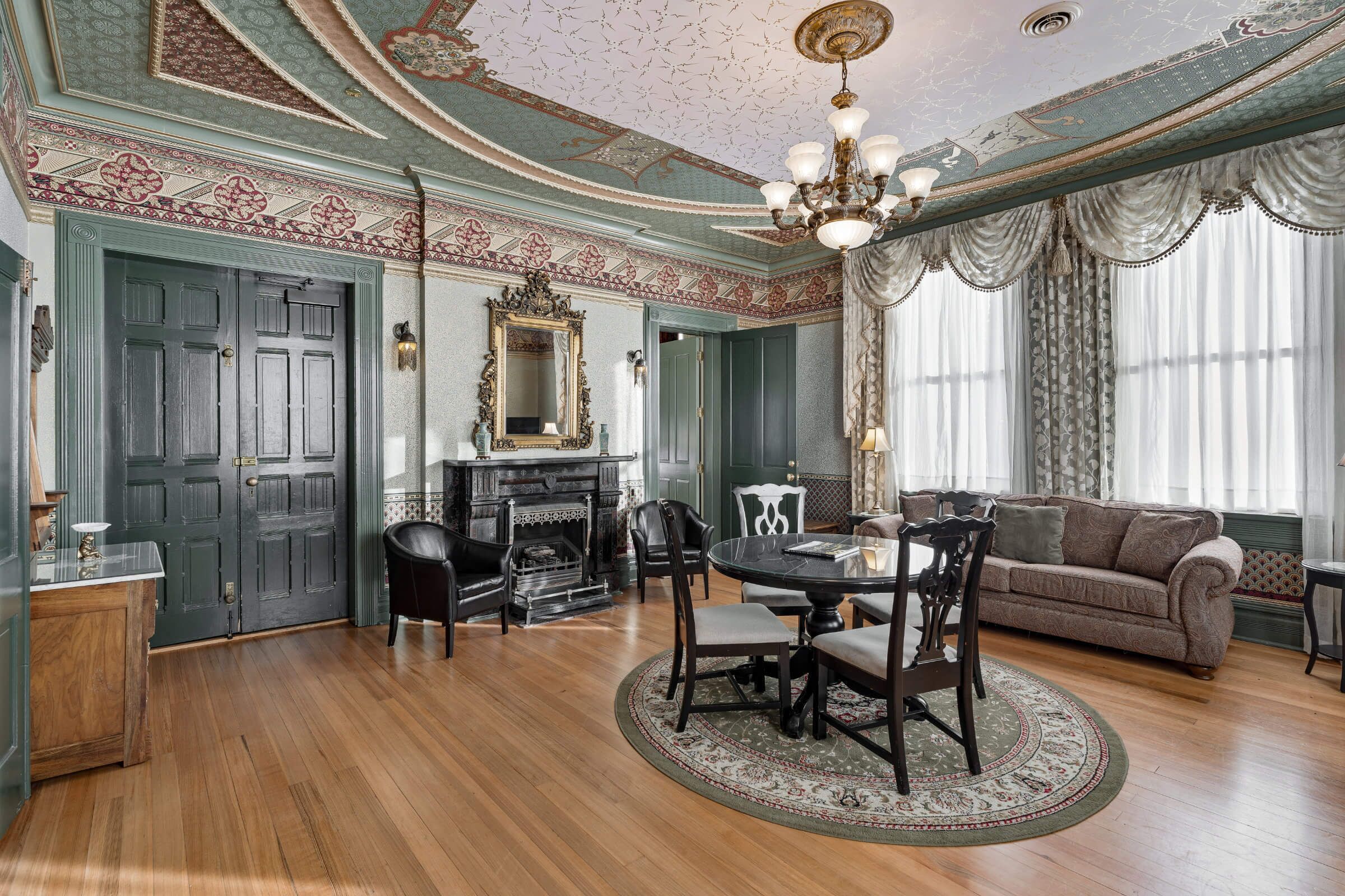 A room with a wooden floor, a dining table with chairs, a sofa, a fireplace, and a chandelier.