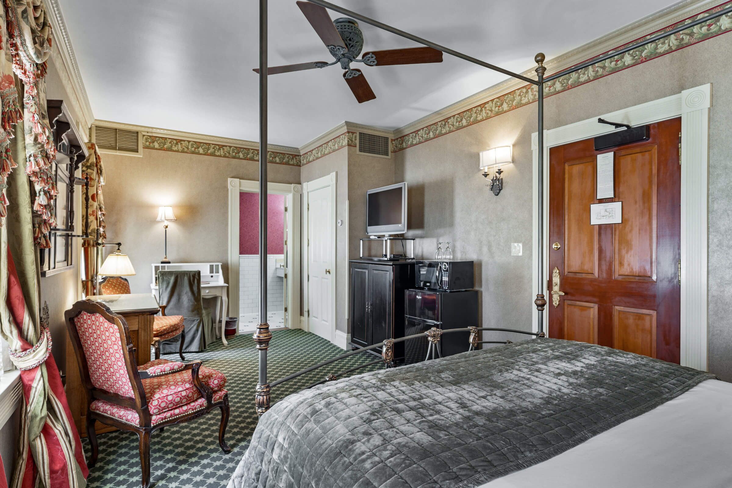 A hotel room with a bed, a desk with a lamp, a chair, a television, and a wardrobe.