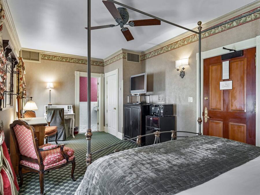 A hotel room with a bed, a desk with a lamp, a chair, a television, and a wardrobe.