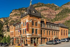 A historic hotel with a prominent clock tower, situated in a mountainous area with a clear view of the surrounding cliffs. - Beaumont Hotel & Spa - Adults Only (Ouray)