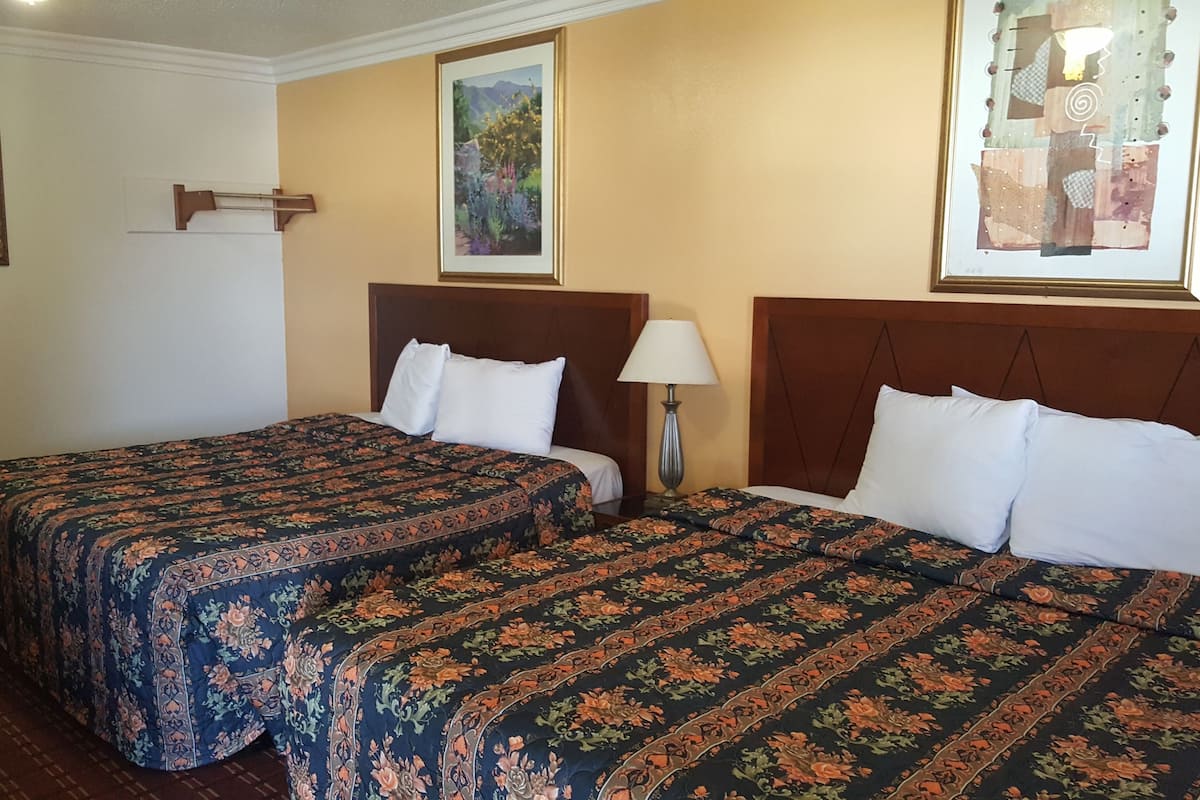 A hotel room with two beds, floral bedspreads, a wooden headboard, a nightstand with a lamp, and framed artwork on the walls.