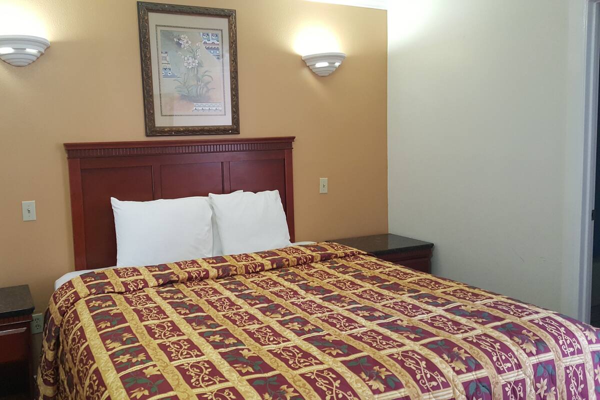 A hotel room with a large bed, a wooden headboard, two bedside tables, a telephone, and a framed picture on the wall.