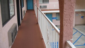 A corridor with a red carpet, a blue door, and a white railing. - Royal Inn Motel Long Beach (Long Beach)