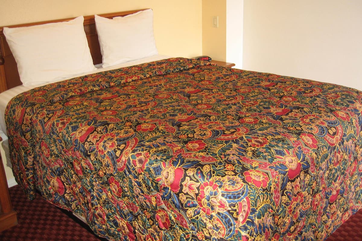 A bed with a colorful patterned bedspread, a white pillow, and a wooden headboard.