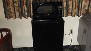 A black refrigerator with a microwave on top, a wooden chair, and a television. - Royal Inn Motel Long Beach (Long Beach)