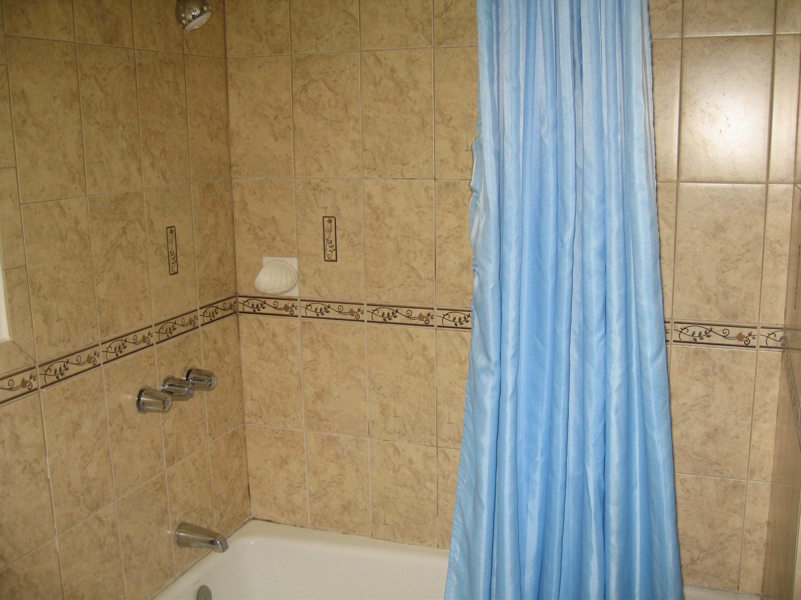 A bathroom with beige tiles, a white bathtub, a blue shower curtain, and a toilet.