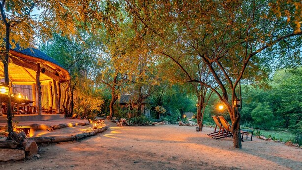 A rustic wooden structure with a thatched roof, surrounded by trees and a dirt path. - Umlani Bushcamp - Lodge (Bushbuckridge)