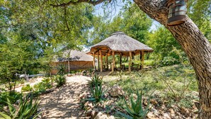 A rustic gazebo with a thatched roof, surrounded by a garden with various plants and rocks. - Umlani Bushcamp - Lodge (Bushbuckridge)