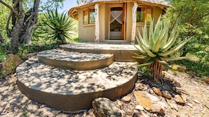 A thatched-roof structure with a door and windows, surrounded by natural vegetation and a stone staircase. - Umlani Bushcamp - Lodge (Bushbuckridge)