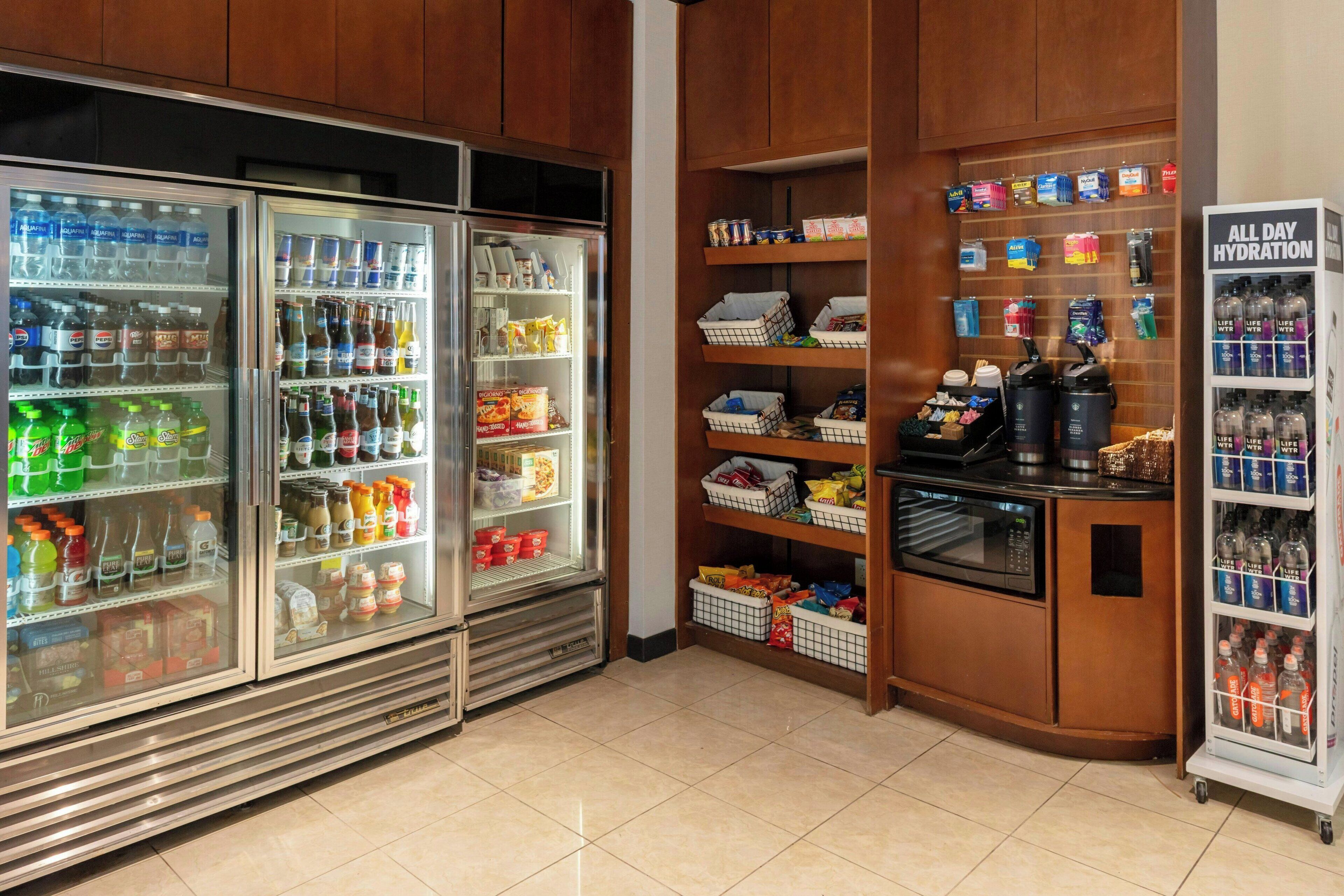 A self-service beverage station with refrigerated drink dispensers and shelves stocked with snacks and bottled water.