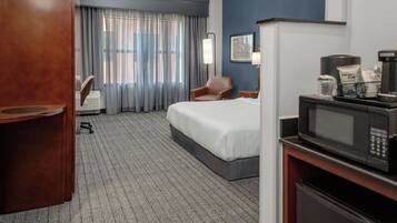 Une chambre d’hôtel équipée d’un lit, d’un bureau avec un ordinateur, d’une chaise, d’un four à micro-ondes et d’une machine à café.