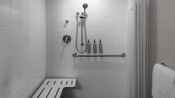 A small, white-tiled bathroom with a shower, a towel rack, and a handrail.