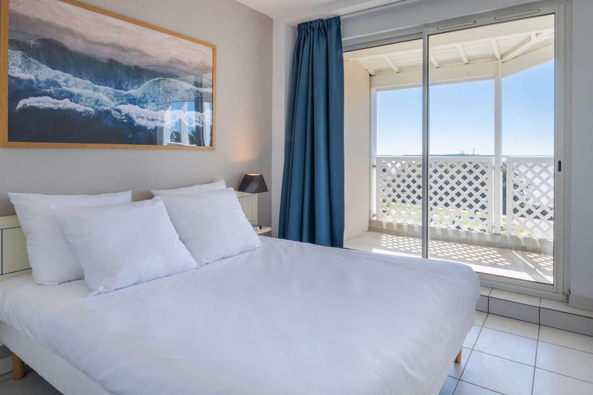 Une chambre d’hôtel avec un grand lit, une table de chevet, une lampe, un tableau et un balcon avec vue.