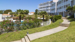 A hotel with a white facade, multiple balconies, and a landscaped garden with palm trees and flowers. - Résidence Odalys Les Terrasses de Fort Boyard (Fouras)