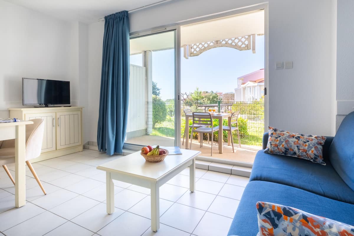 Un salon moderne comprenant un canapé, un téléviseur, une table à manger et un balcon aménagé avec du mobilier d’extérieur.