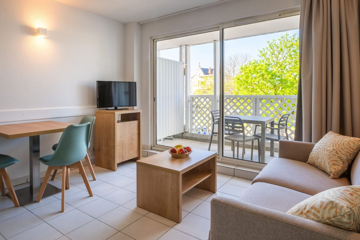 Un salon moderne comprenant un canapé, une table basse, un téléviseur et un balcon aménagé avec du mobilier d’extérieur.