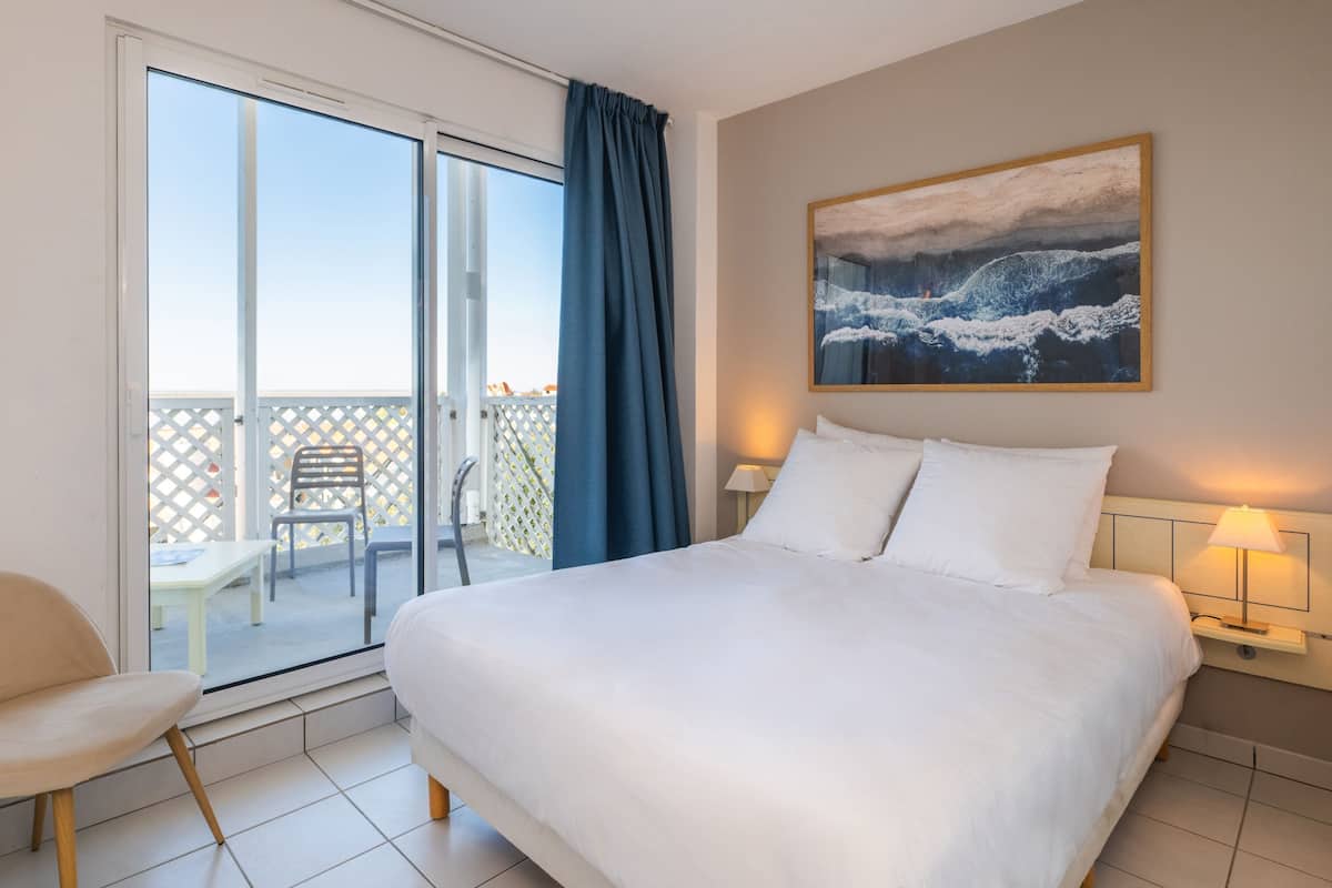 Une chambre d’hôtel avec un grand lit, un balcon avec vue et un tableau au mur.