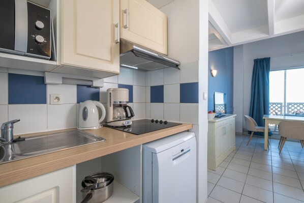 A compact kitchen with a sink, stove, and a compact dishwasher. There is a dining area with a table and chairs. - Résidence Odalys Les Terrasses de Fort Boyard (Fouras)